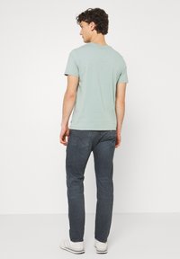 T-shirt de algodão verde claro com mangas curtas, combinado com jeans de denim escuro. Ténis brancos e detalhe minimalista de costura no bolso traseiro.