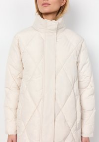Licht beige gewatteerde jas met een hoge kraag, voorzien van een ruitpatroon, een zachte textuur en een centrale sluiting.