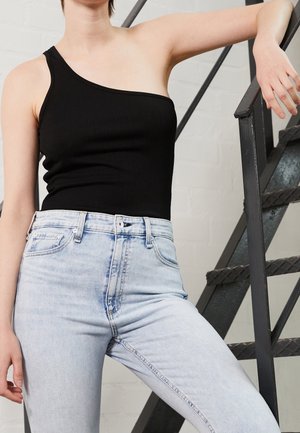 Schwarzes, einseitig-tragendes, geripptes Tanktop, kombiniert mit hellblauen, hoch taillierten Jeans. Der Stoff ist glatt und hat eine figurbetonte Silhouette.