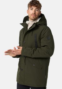 Dark green parka jacket with a hood, featuring a zip and button closure, large front pockets, and contrasting black accents. Textured fabric.