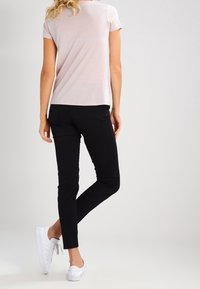 Svetle růžové tričko s krátkým rukávem, černé slim-fit kalhoty a bílé tenisky. Hladká textura, ležérní design, viditelné švy a měkká látka.