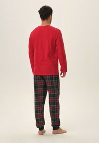 Czerwona bluzka z długim rękawem zestawiona z spodniami w kratę w kolorze zielonym, czerwonym i białym. Spodnie mają elastyczny pasek w talii i zakończenia w formie ściągaczy.