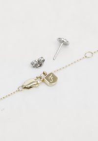 Bracciale in oro con chiusura, dotato di un charm esagonale inciso con la lettera "F". Include un orecchino a manchetto in argento e un orecchino a perno con una gemma.
