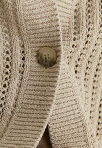 Beige knitted cardigan with ribbed trim and large marbled button, featuring openwork knit pattern on textured fabric.