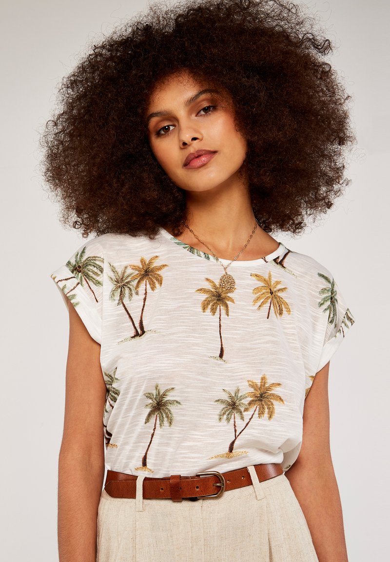 White short-sleeve shirt with a palm tree print in green and yellow hues, paired with a brown leather belt and beige pants.