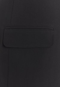 Czarna tkanina z płaską kieszenią naszywaną i klapką złożoną, gładką teksturą oraz czystym przeszyciem wzdłuż krawędzi.