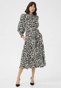 Midi-jurk met luipaardprint, een aansluitende taille, lange mouwen en zakken. De stof is glad met zwart en beige kleuren. Zwarte hakken maken de look compleet.