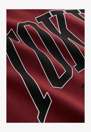 Bordowy materiał z dużymi czarnymi literami blokowymi obramowanymi na biało, układającymi się na powierzchni w słowo "YORK".