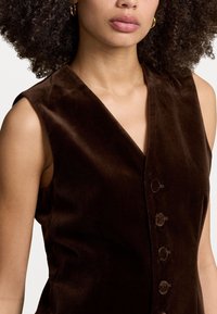 Brun sammet ärmlös klänning med v-ringning, fem matchande knappar framtill och en mjuk textur.