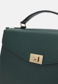 Zielona torebka o fakturowanej powierzchni i strukturalnym kształcie, z złotym zamknięciem na zatrzask i zaokrąglonym uchwytem. Gładka powierzchnia i minimalistyczny design.