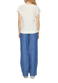 Weißes Kurzarmhemd mit lockerer Passform, kombiniert mit lockeren blauen Jeans. Das Hemd hat eine glatte Textur und ein schlichtes Design.