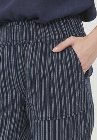 Tengerészkék csíkos nadrág gumis derékkal, függőleges fehér és világosszürke csíkokkal, oldalsó zsebekkel. Puha tapintású.