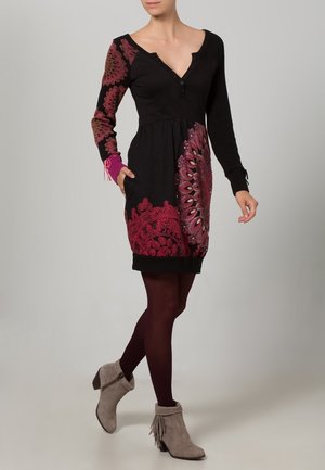 Černé šaty s dlouhými rukávy, růžovými a vínovými květinovými vzory, žebrovanými manžetami a výstřihem do oblouku; doplněné šedými kotníkovými botami.