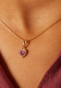 Gouden ketting met een hartvormige hanger met een centrale roze edelsteen omringd door kleine heldere stenen.