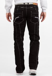 Jeans in denim nero con cuciture bianche a contrasto, cinque tasche e vestibilità affusolata. Presenta passanti per cintura visibili e una patta in pelle con il marchio.