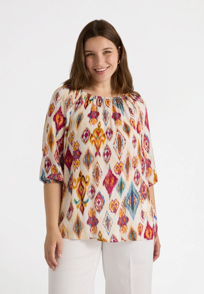 Bluzka w kwiatowy wzór z okrągłym dekoltem, krótkimi elastycznymi rękawami oraz wielokolorowymi diamentami na kremowym tle.