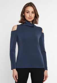 Dunkelblaues Rollkragenoberteil mit Cutouts an den Schultern, langen Ärmeln und einer glatten Stofftextur. Enganliegendes Design.