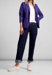 Fioletowa marynarka na białej koszulce, zestawiona z ciemnoniebieskimi, podwiniętymi dżinsami i jasnobeżowymi trampkami. Gładki materiał, strukturalny krój.