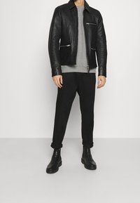 Zwarte leren jas met ritszakken, grijze sweatshirt eronder, zwarte broek en zwarte laarzen. Gladde textuur, op maat gemaakte pasvorm.