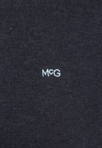 Navy blue knitted fabric with a fine texture featuring white embroidered letters "MCG" on the lower right corner.