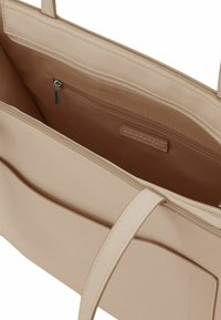 Intérieur d'un sac fourre-tout beige avec une texture lisse, comprenant une poche zippée et deux compartiments ouverts, le tout dans une harmonie de couleurs.