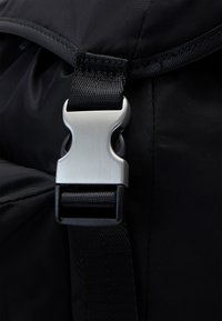 Correa de mochila de nylon negro con hebilla de metal plateado, correa texturizada y detalles de costura para mayor durabilidad.