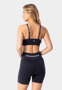 Soutien-gorge de sport noir et short taille haute. Le soutien-gorge a des bretelles réglables et un logo ; le short présente une taille épaisse avec un marquage. Texture douce.