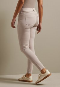 Světle růžové skinny džíny s vysokým pasem a dvěma zadními kapsami, v kombinaci s krémovými nízkými teniskami s hnědou podrážkou.