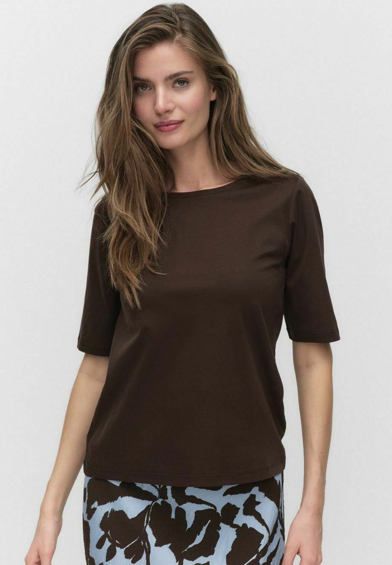 T-shirt marron à manches courtes avec un col rond, en tissu doux. Associé à une jupe bleu et noir à motifs floraux.
