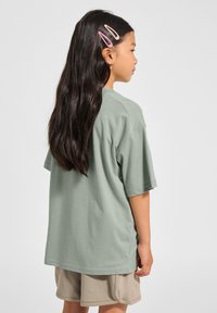 Ljusgrön bomullströja med korta ärmar, avslappnad passform och rund hals. Matchad med beige shorts och hårklämmor.