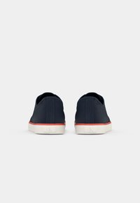 Navy canvas sneakers with a white rubber sole and red accent stripe. Clean, minimal design with a textured finish and subtle logo detail.