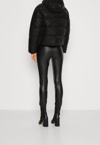 Veste matelassée noire brillante avec capuche, associée à un pantalon noir en similicuir moulant et des bottines à talons épais.