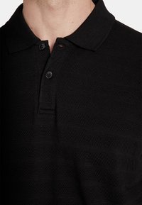 Czarna koszulka polo z teksturowanym wzorem, z kołnierzykiem i dwoma guzikami. Materiał ma paskowany wzór i miękką teksturę.