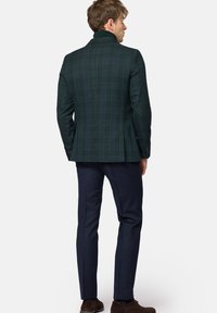 Zielona marynarka w kraciasty wzór z wysokim kołnierzem i wyraźnie zarysowanymi ramionami. Połączona z granatowymi spodniami i brązowymi butami, co podkreśla dopasowany krój.