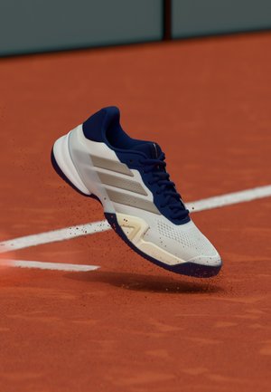 Witte en marineblauwe tennisschoen met een lichtgewicht mesh bovenwerk, gestructureerd oppervlak, rubberen zool en drie parallelle strepen aan de zijkant.