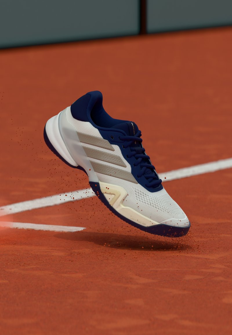 Chaussure de tennis blanche et marine avec une tige en mesh léger, une surface texturée, une semelle en caoutchouc et trois bandes parallèles sur le côté.