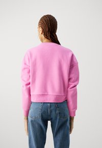 Sudadera corta rosa con cuello redondo y hombros caídos, combinada con jeans de tiro alto azules. Textura de tejido suave.