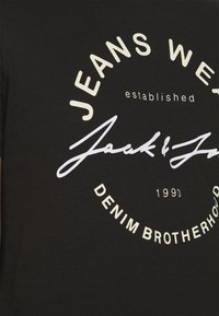 Camiseta de algodón negra con un diseño gráfico redondo que presenta el texto "JEANS WEAR", "Jack & Jones" y "DENIM BROTHERHOOD 1990" en color blanco y crema.