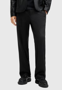 Pantalones negros con un diseño de pierna recta, hechos de una tela suave. Combinados con una chaqueta de cuero negra y zapatos negros. Sin patrones ni acentos.