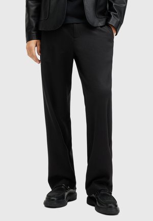 Pantaloni neri con una silhouette a gamba dritta, realizzati in un tessuto morbido. Abbinati a una giacca di pelle nera e scarpe nere. Nessun motivo o dettaglio decorativo.