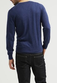 Marineblauer Pullover aus weichem Strickstoff, mit Rundhalsausschnitt, langen Ärmeln und fitted Saum. Kombiniert mit dunklen Jeans.