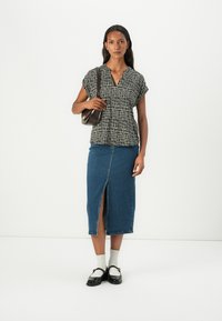 Black and white patterned short-sleeve top with a V-neck, paired with a mid-length denim skirt featuring a front slit. Black shoes and socks complete the look.