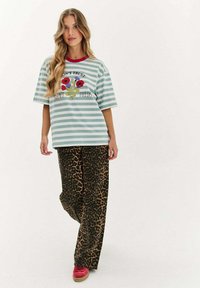 Pruhované zelené oversized tričko s květinovou grafikou, spárované s volnými kalhotami s leopardím potiskem a červenými botami. Neformální streetwear outfit.