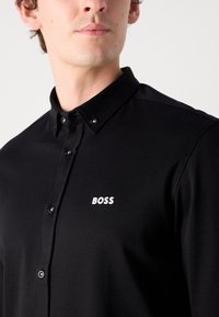 Zwarte button-up shirt van soepele stof, met een klassieke kraag, subtiele logo borduursel in het wit en zwarte knopen.