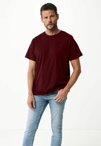 Bordowa koszulka z miękkiego materiału, z okrągłym dekoltem i krótkimi rękawami. Do kompletu jasnoniebieskie obcisłe jeansy, minimalne oznaczenia marki.