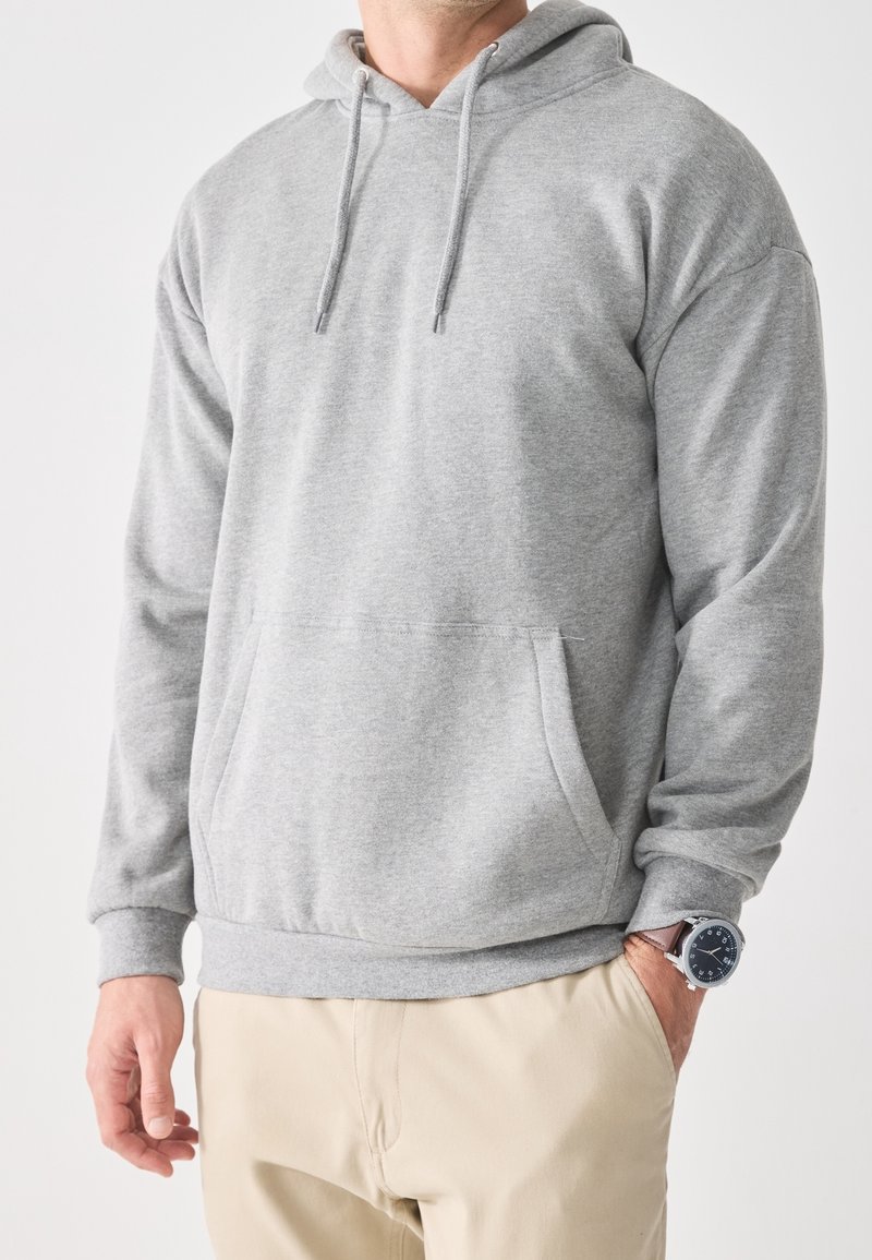 Felpa grigia con cappuccio realizzata in tessuto morbido, dotata di tasca a marsupio, polsini a coste e coulisse per una vestibilità regolabile.