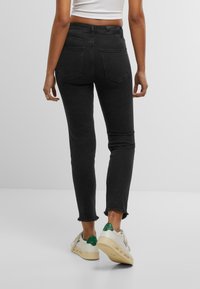 Upravené černé džíny s vysokým pasem, roztrhaným lemem a dvěma zadními kapsami, doplněné o bílé tenisky s zelenými detaily.