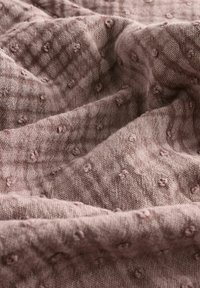 Textured cotton fabric in soft mauve tone, featuring a checkered pattern and raised bobble accents, creating depth and visual interest.