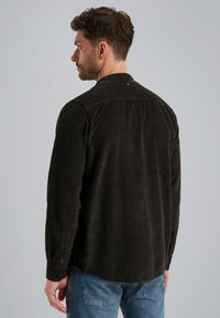 Camisa de pana verde oscuro con mangas largas, puños abotonados y un cuello clásico. Presenta una superficie texturada con costillas y un detalle en el yugo trasero.