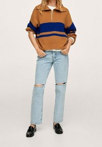 Pull zippé marron avec des rayures bleues, associé à un jean déchiré bleu clair et des mocassins noirs. Texture en mélange de coton. Design décontracté.